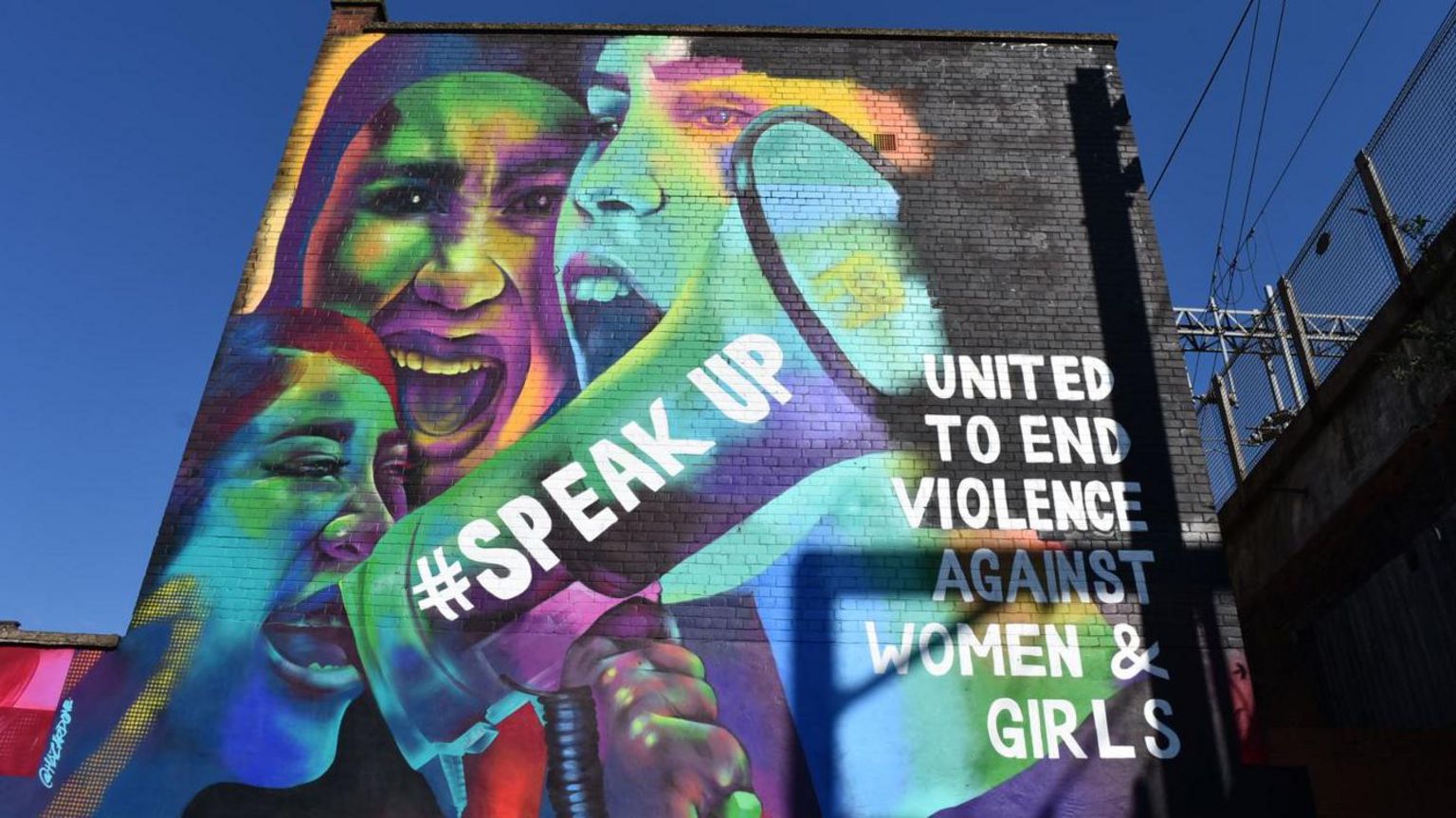 A mural of women with a megaphone which says 'speak up' and text which says 'united to end violence against women and girls'