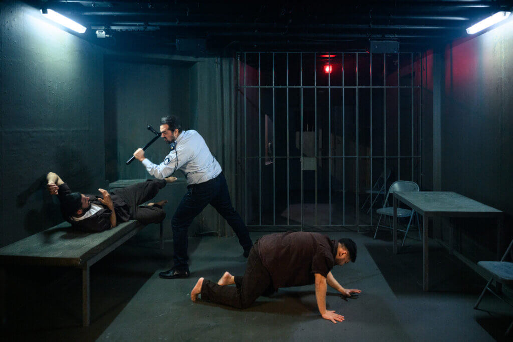 A still from Prisoners of the Occupation in Denmark, with Arian Kashef (l), Wahid Sui Mahmoud (r) and Martin Hylander (c). The scene shows an Israeli prison guard beating two Palestinian prisoners with a club. (Photo by Søren Meisner of Teater Gaius)