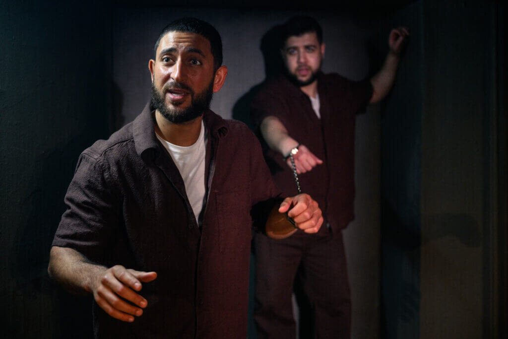 A still from Prisoners of the Occupation in Denmark, with Arian Kashef (l) and Wahid Sui Mahmoud (r). The scene shows two Palestinian prisoners who are shackled together. (Photo by Søren Meisner of Teater Gaius)