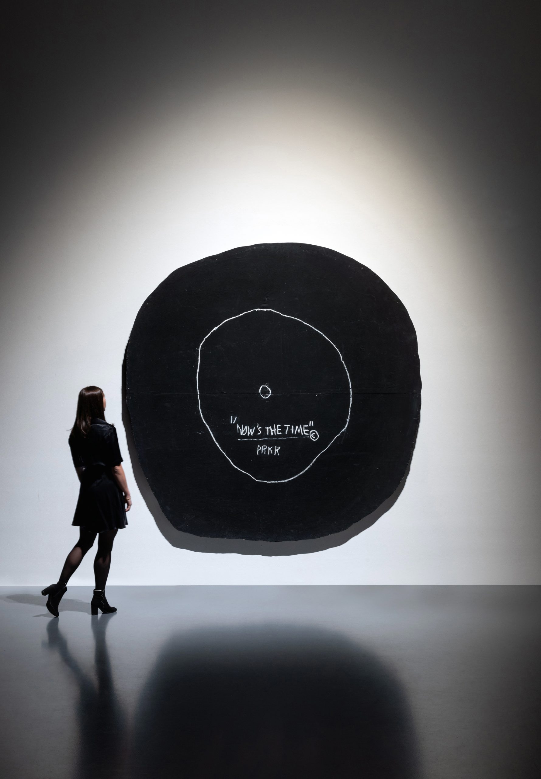 A person looking at a large painting resembling an abstracted version of a vinyl record.