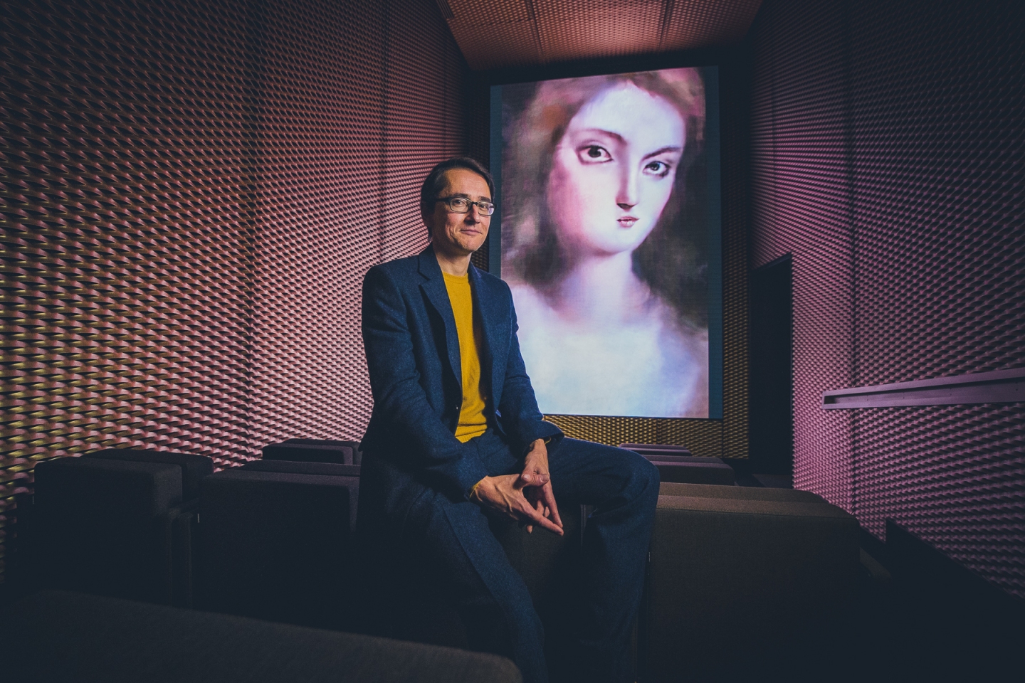 Mario Klingemann sits in front of one of his A.I.-generated portraits.