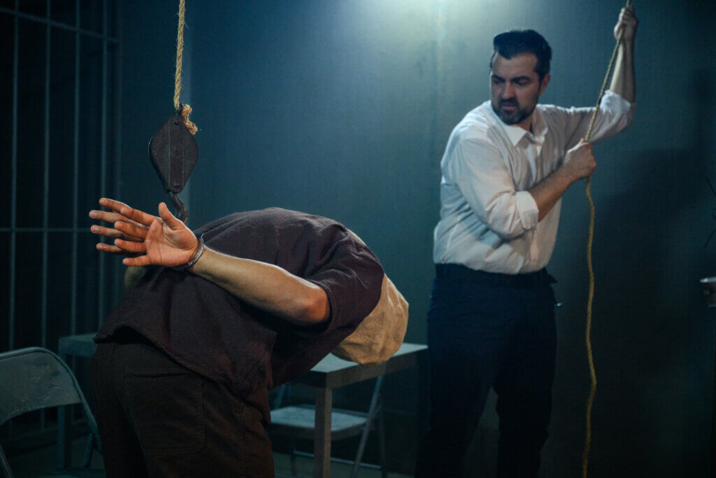 A scene from Prisoners of the Occupation in Denmark, with Wahid Sui Mahmoud (l) and Martin Hylander. The scene shows a Palestinian prisoner being tortured in a stress position by an Israeli prison guard. (Photo by Søren Meisner, Teater Gaius)