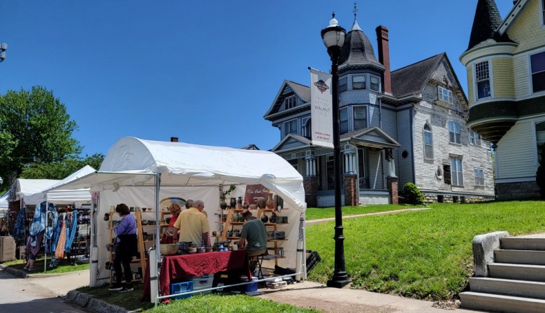 A white tent selling art is set up in front of a historic Victorian home