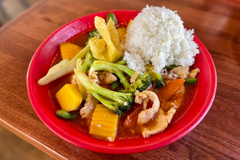 A red plate of Thai food, sitting on a brown wooden table