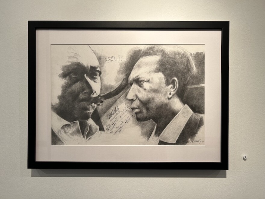 A black and white pencil drawing is matted and framed in a gallery. It shows two views of legendary musician John Coltrane's face.