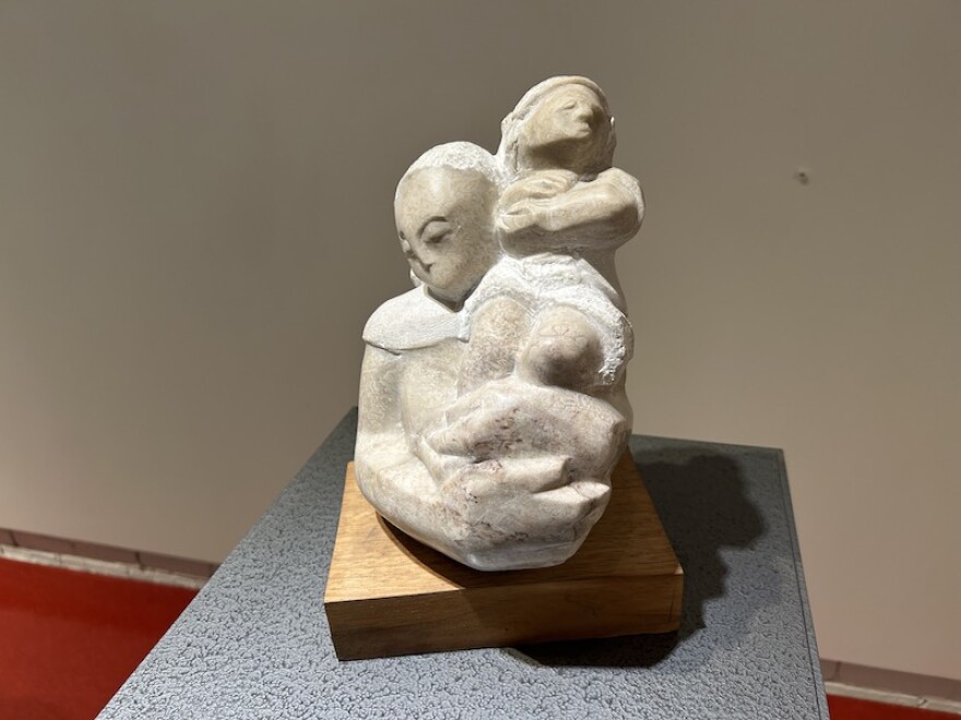 A small stone sculpture sits on a plinth. It depicts a woman holding a child.
