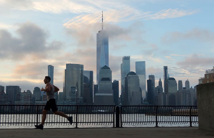 A person runs in front of the skyline of lower Manhattan and One World Trade Center in New York City as the sun rises on August 29, 2023, as seen from Jersey City, New Jersey.