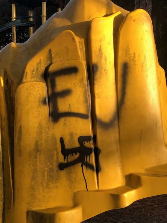 yellow piece of playground equipment vandalized with Nazi graffiti, including a swastika and an 