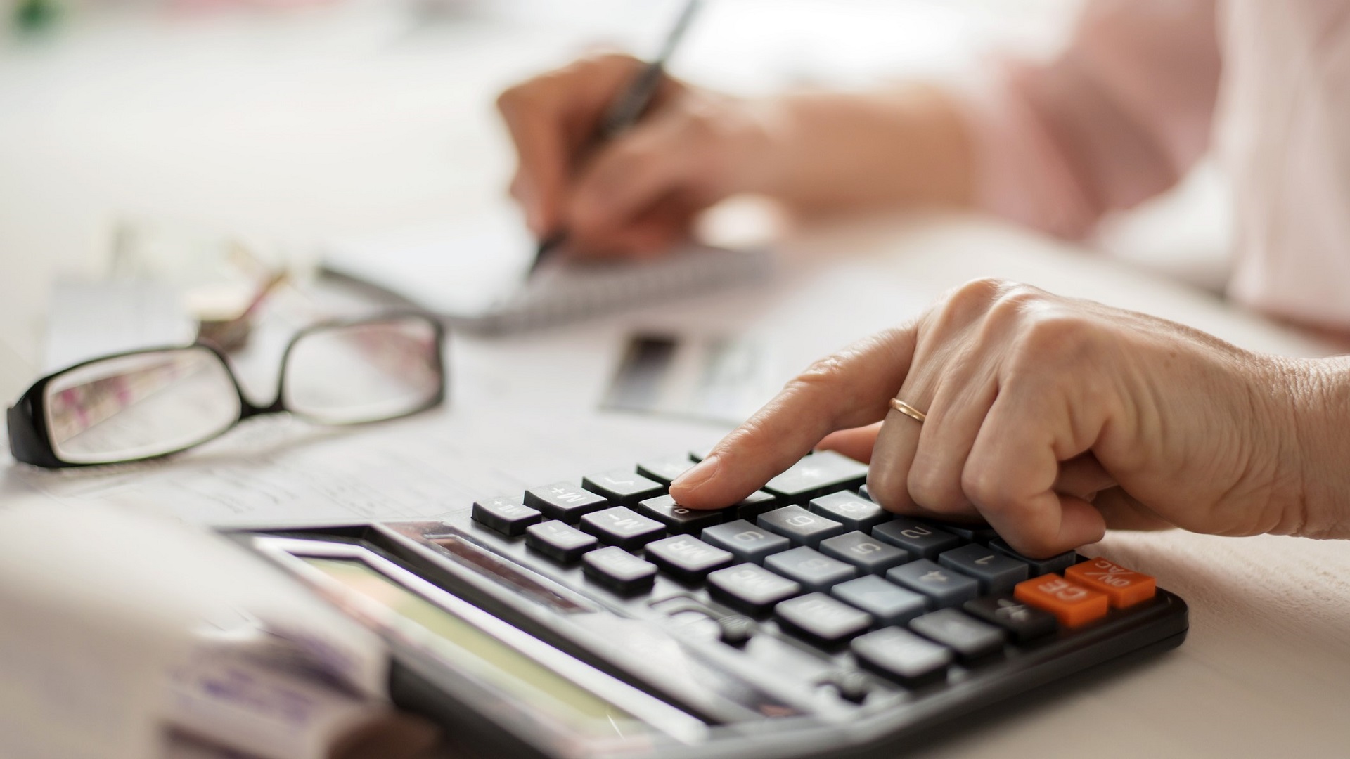 Pension calculation concept, old hands counting finances on a home calculator , close- up stock photo
